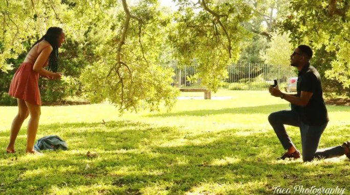 Samuel on one knee proposing to Oneisha under an oak tree